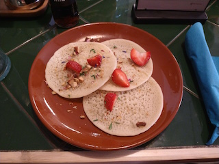 A photo of 3 Moroccan pancakes on a plate. The pancakes have strawberries, nuts and herbs on them.