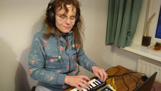 A photo of isocosa with headphones on, using a MIDI keyboard plugged into a laptop.